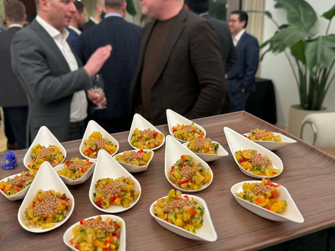 Plateau de bouchées au premier plan et invités échangeant lors d’une réception.